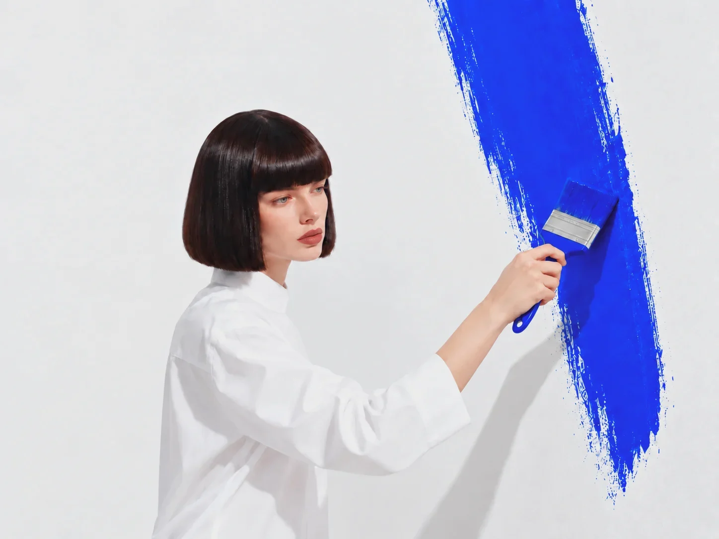 Eine Frau malt einen blauen Pinselstrich auf eine weiße Wand